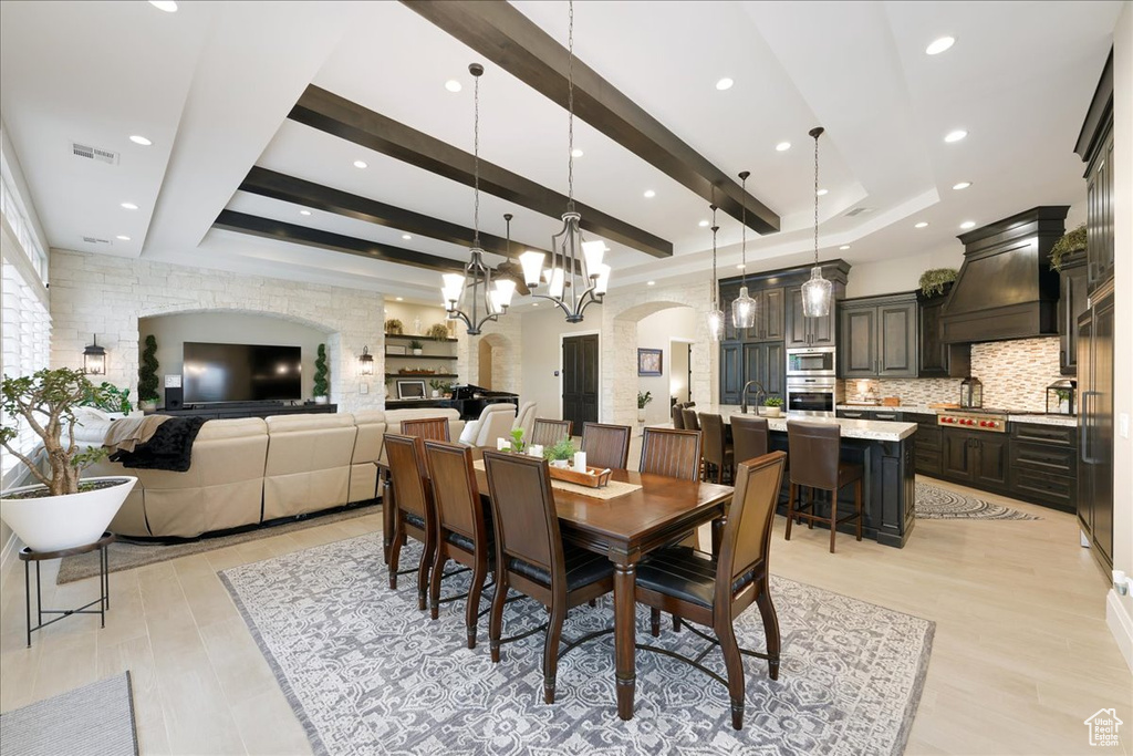 Dining area with light hardwood / wood-style flooring, a notable chandelier, beamed ceiling, and sink