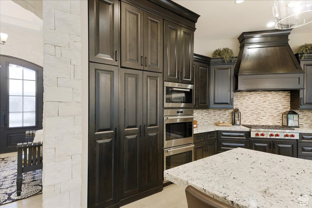 Kitchen featuring appliances with stainless steel finishes, premium range hood, tasteful backsplash, and hanging light fixtures