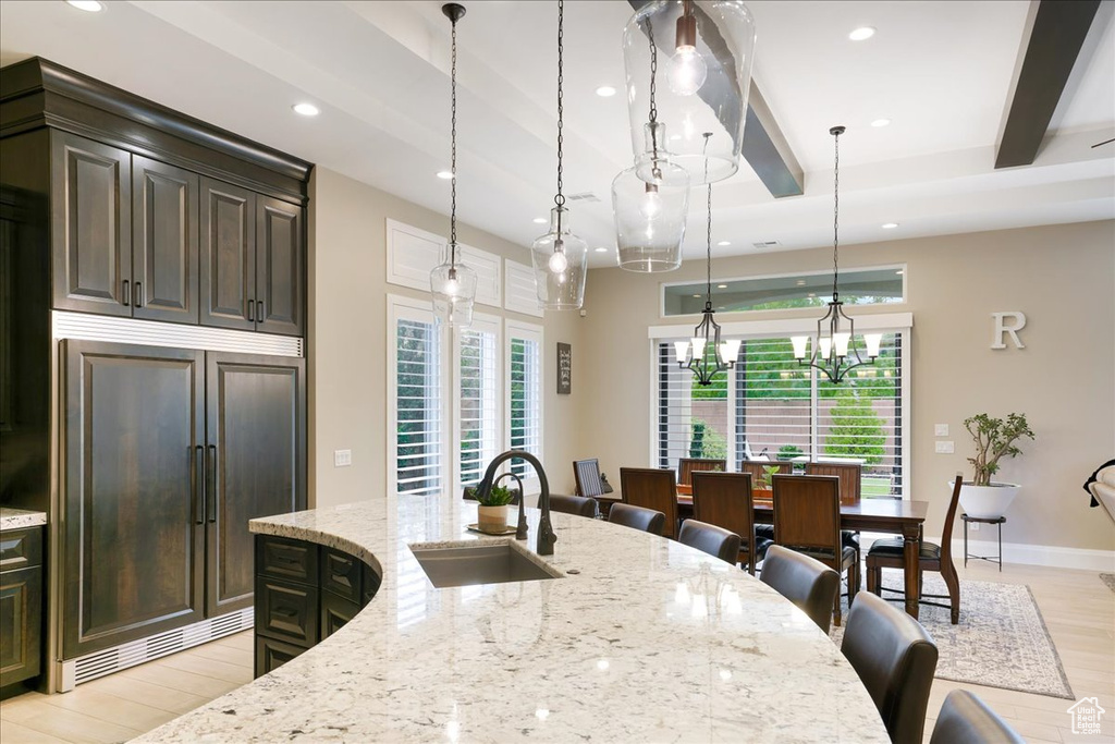 Kitchen featuring hanging light fixtures, light stone countertops, light wood-type flooring, beam ceiling, and sink