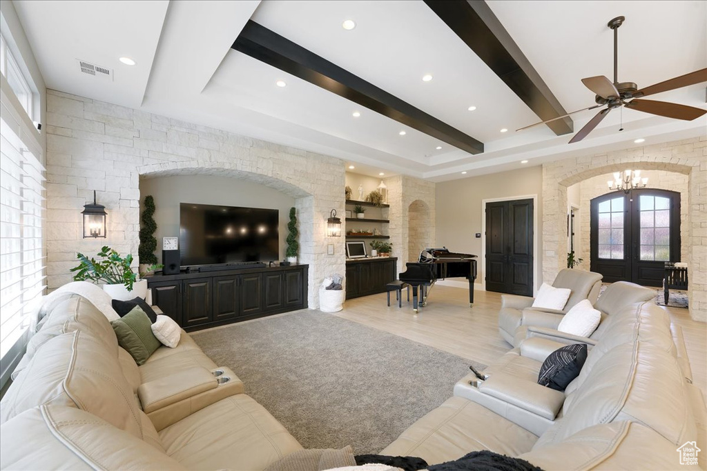 Living room with ceiling fan with notable chandelier, light wood-type flooring, beamed ceiling, and french doors