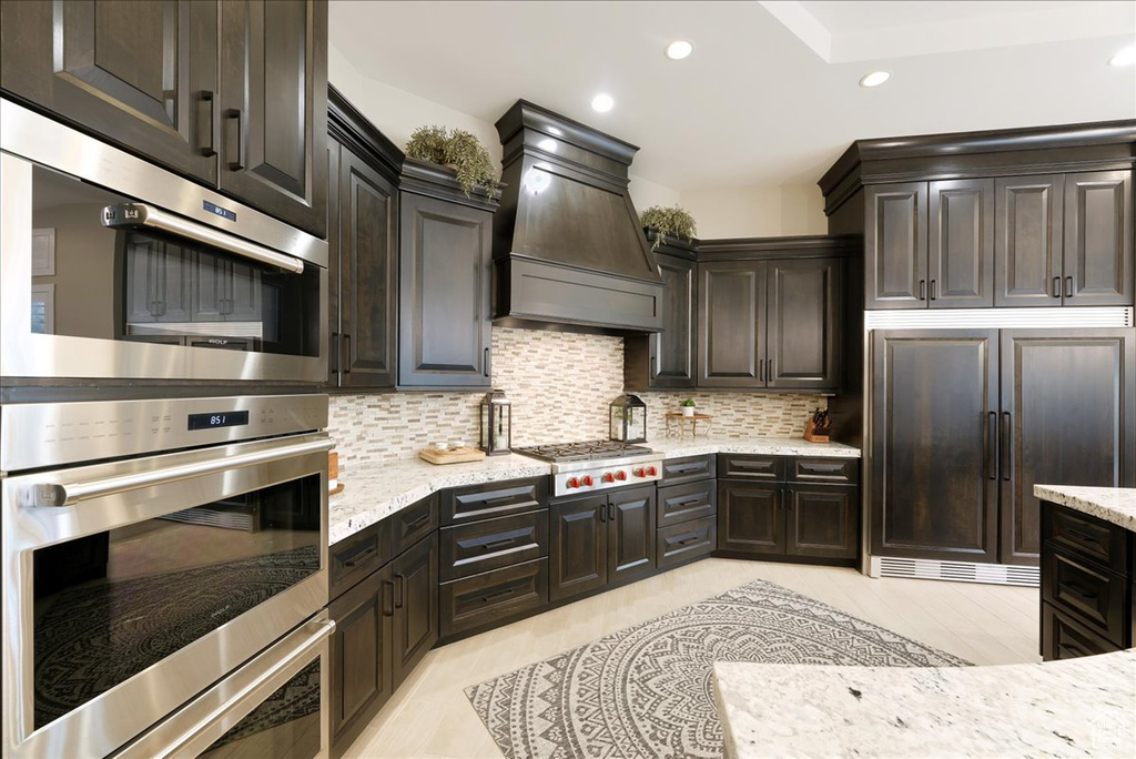 Kitchen with light stone countertops, stainless steel appliances, custom range hood, and tasteful backsplash