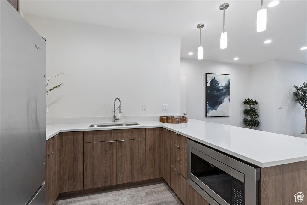 Kitchen with pendant lighting, light hardwood / wood-style floors, sink, kitchen peninsula, and appliances with stainless steel finishes