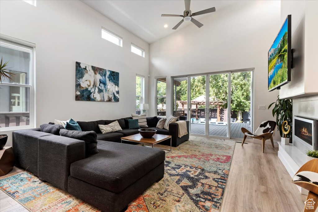 Living room with ceiling fan, light wood-type flooring, and a high ceiling