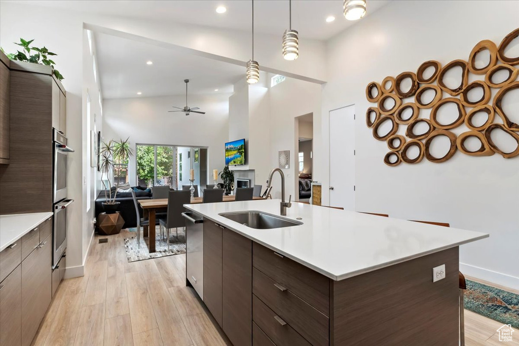 Kitchen featuring dark brown cabinets, light hardwood / wood-style floors, sink, high vaulted ceiling, and decorative light fixtures