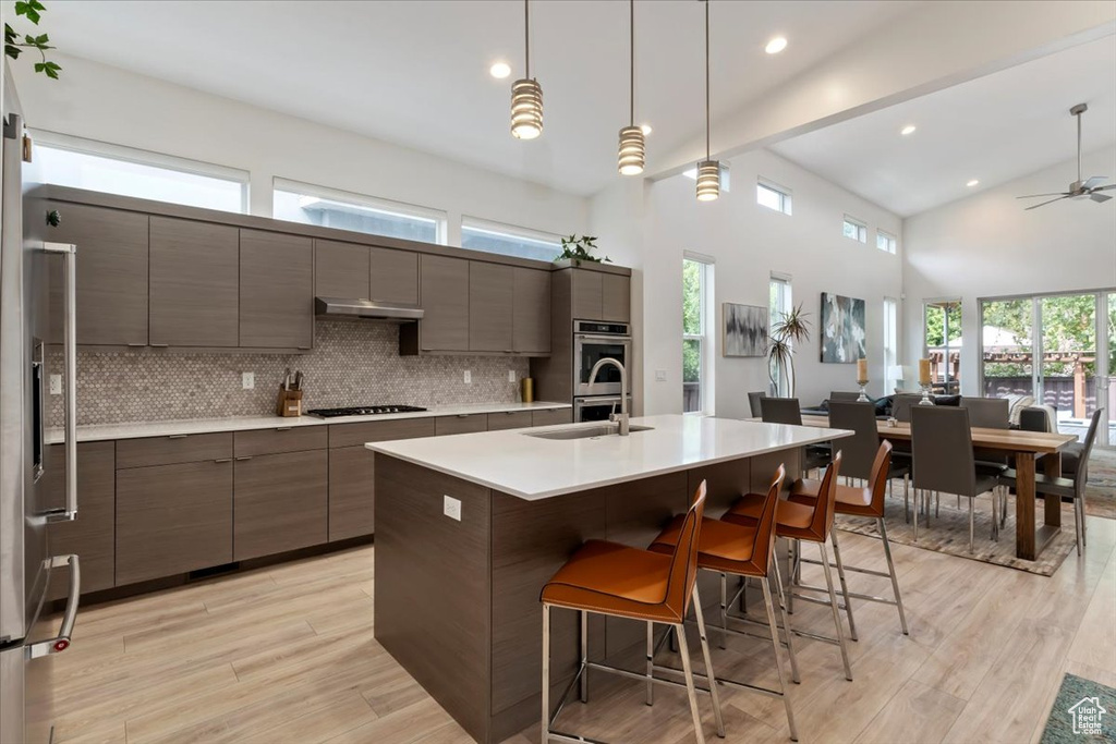 Kitchen with light hardwood / wood-style floors, a kitchen bar, stainless steel appliances, and tasteful backsplash