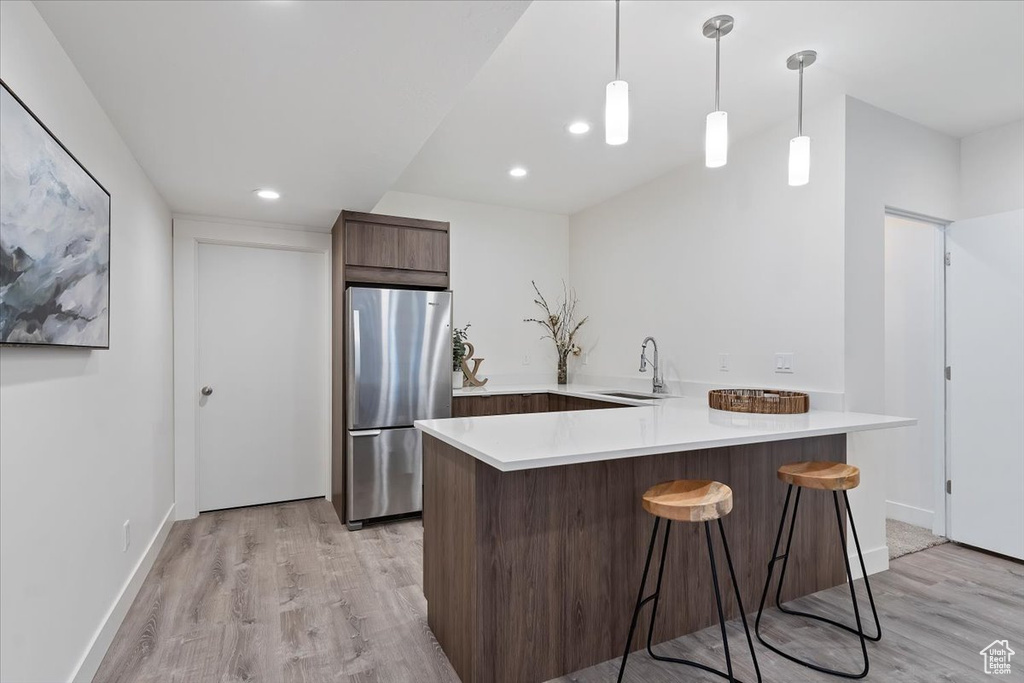 Kitchen featuring hanging light fixtures, stainless steel fridge, sink, light hardwood / wood-style flooring, and a kitchen bar