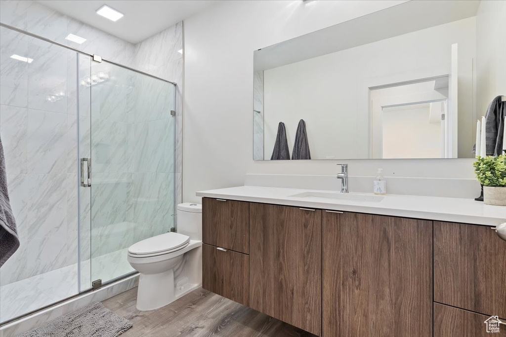 Bathroom with wood-type flooring, vanity, a shower with shower door, and toilet