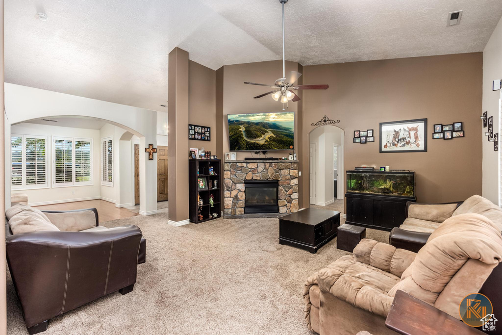 Carpeted living room featuring high vaulted ceiling, a textured ceiling, ceiling fan, and a stone fireplace