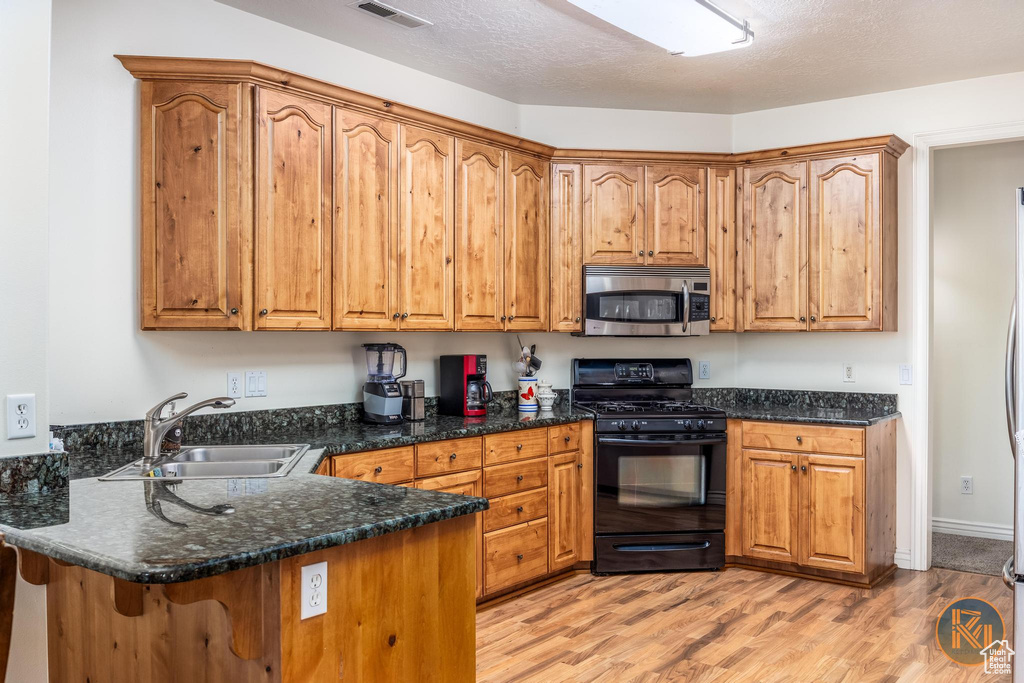 Kitchen featuring light wood-type flooring, a textured ceiling, sink, kitchen peninsula, and black range with gas cooktop