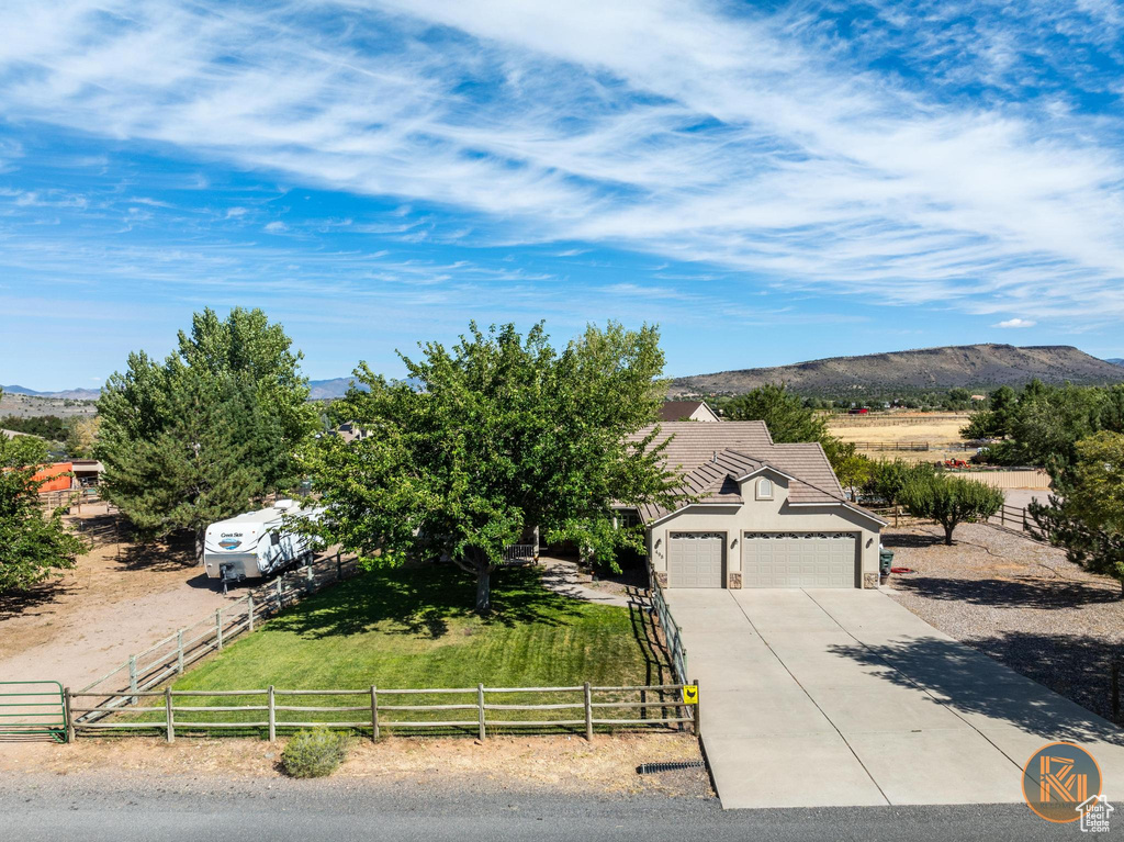 View of front of house featuring a mountain view, a front lawn, a rural view, and a garage