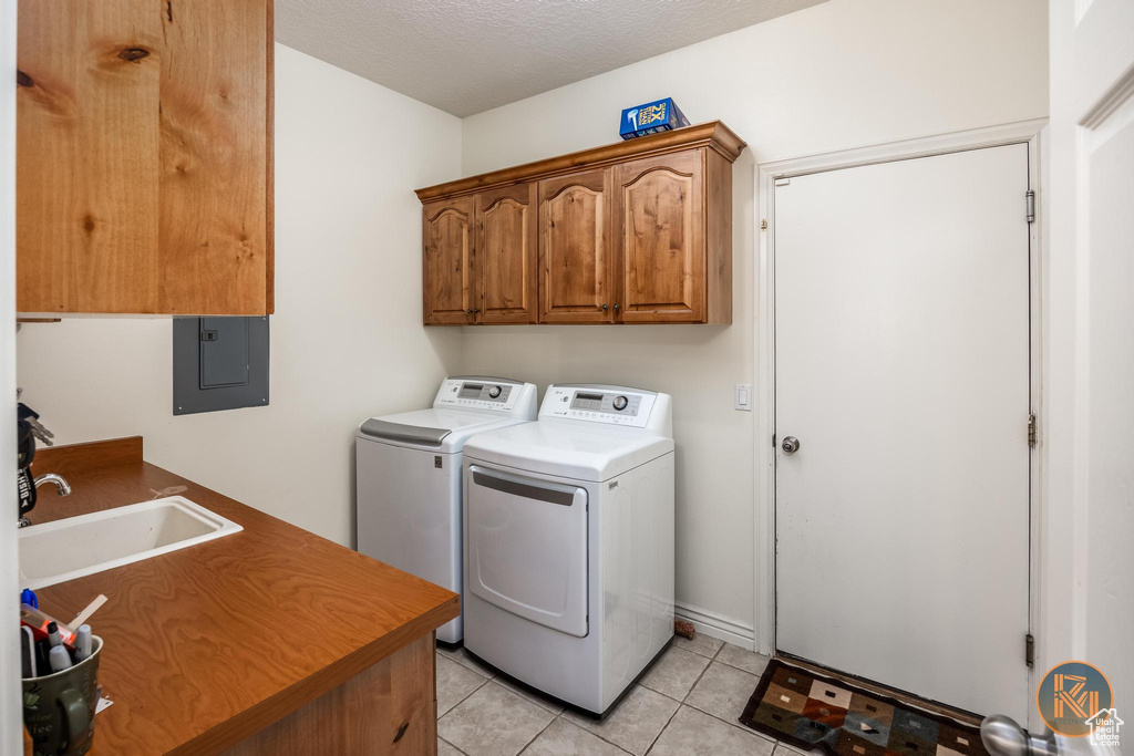 Washroom featuring cabinets, a textured ceiling, electric panel, light tile patterned floors, and separate washer and dryer