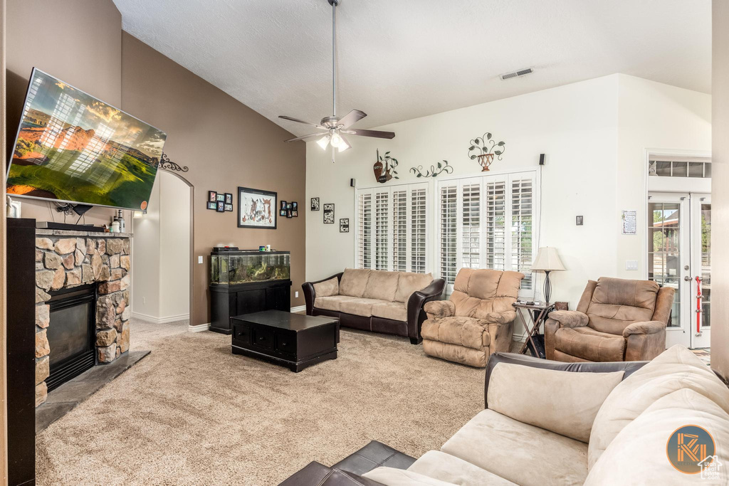 Carpeted living room featuring high vaulted ceiling, ceiling fan, and a stone fireplace