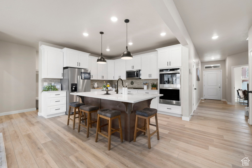 Kitchen featuring hanging light fixtures, a center island with sink, light hardwood / wood-style flooring, and stainless steel appliances