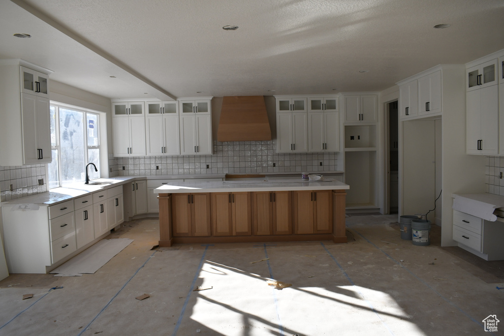 Kitchen featuring sink, a spacious island, white cabinets, premium range hood, and decorative backsplash