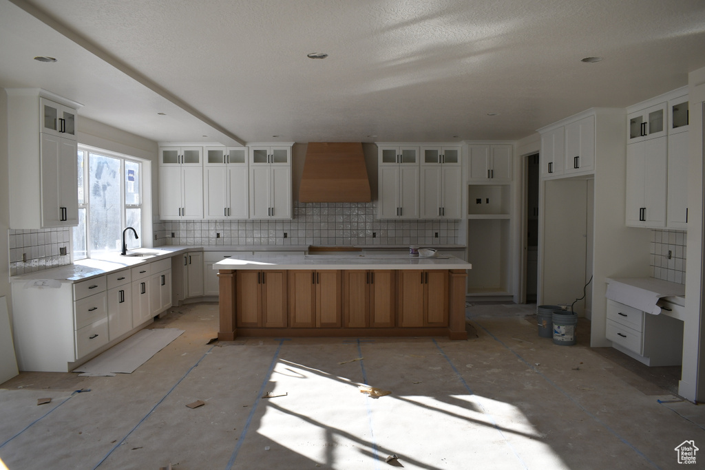 Kitchen with white cabinets, sink, tasteful backsplash, custom exhaust hood, and a spacious island