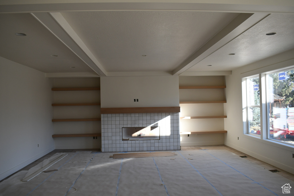 Unfurnished living room featuring a fireplace, a textured ceiling, and beam ceiling