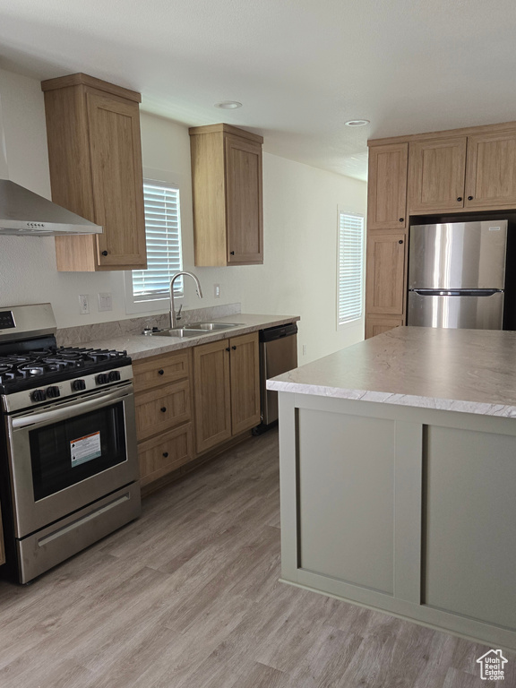 Kitchen featuring appliances with stainless steel finishes, wall chimney exhaust hood, sink, and light hardwood / wood-style flooring