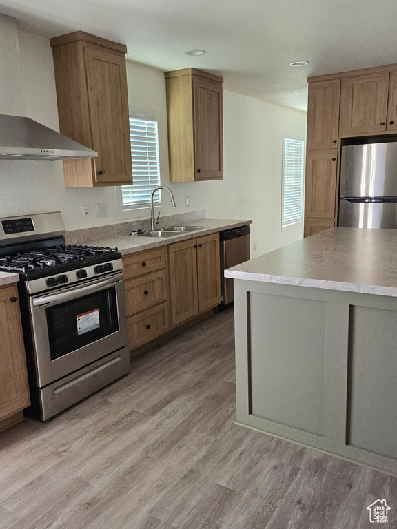 Kitchen featuring light wood-type flooring, appliances with stainless steel finishes, wall chimney exhaust hood, and sink