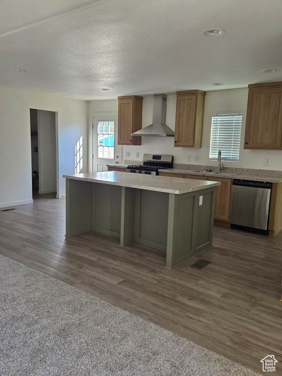 Kitchen with a textured ceiling, dark wood-type flooring, a kitchen island, wall chimney exhaust hood, and stainless steel appliances