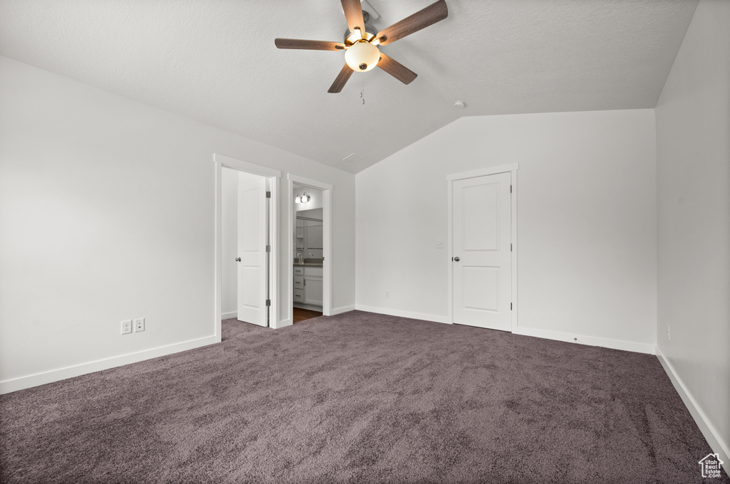 Unfurnished bedroom with ceiling fan, ensuite bath, vaulted ceiling, and dark carpet