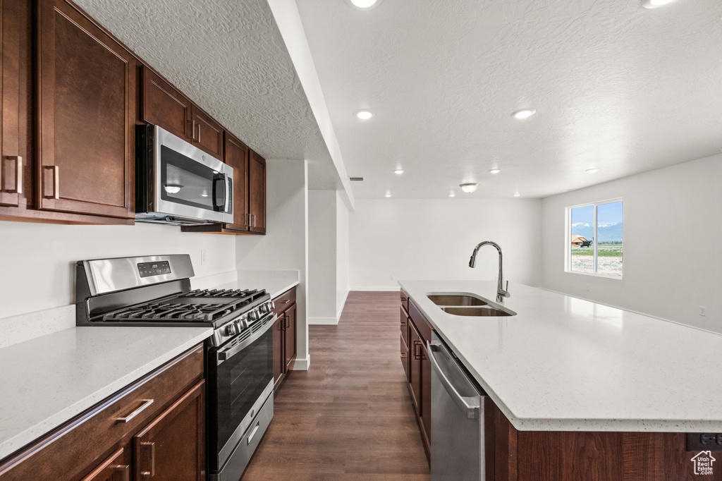 Kitchen with appliances with stainless steel finishes, dark hardwood / wood-style flooring, a textured ceiling, a kitchen island with sink, and sink