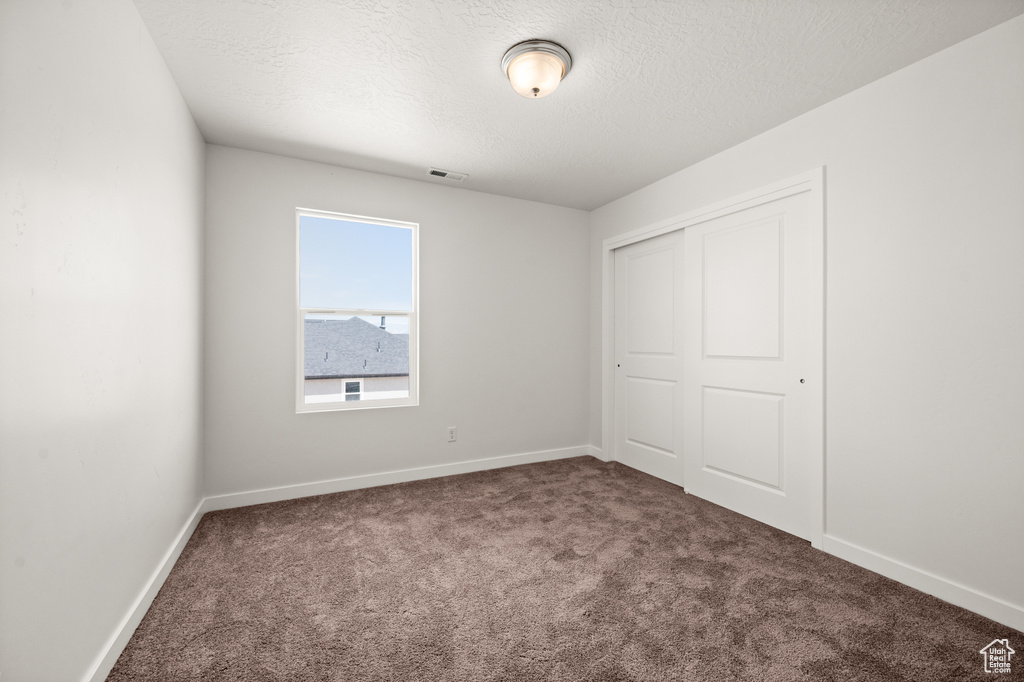 Unfurnished bedroom featuring a textured ceiling, a closet, and dark colored carpet