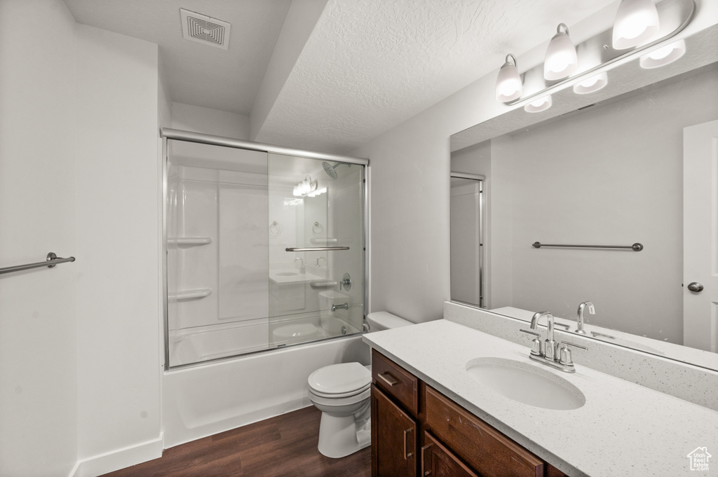 Full bathroom featuring a textured ceiling, shower / bath combination with glass door, hardwood / wood-style flooring, vanity, and toilet