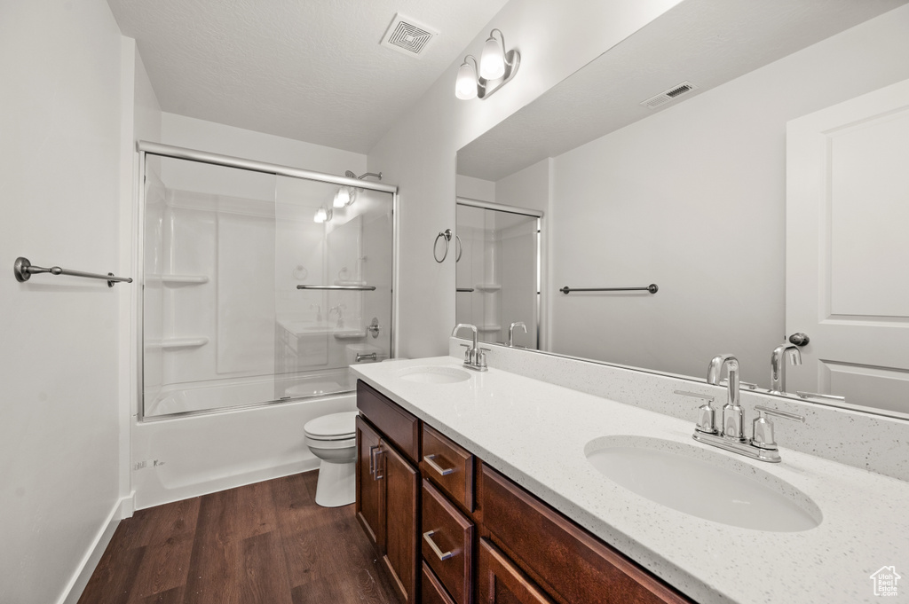 Full bathroom with vanity, hardwood / wood-style flooring, enclosed tub / shower combo, and toilet