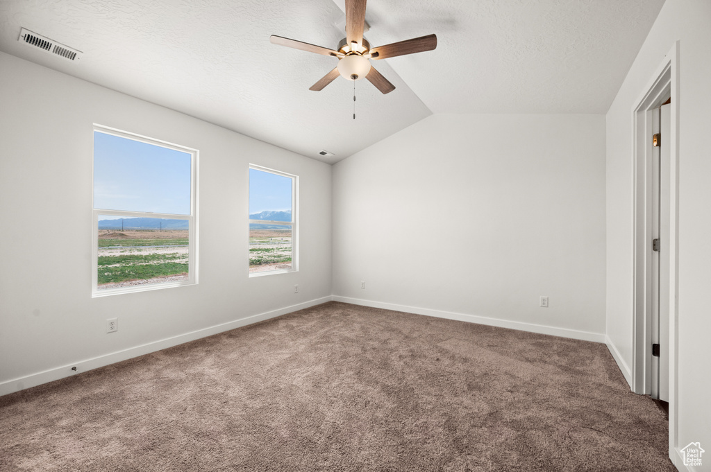 Carpeted empty room with lofted ceiling, ceiling fan, and a textured ceiling