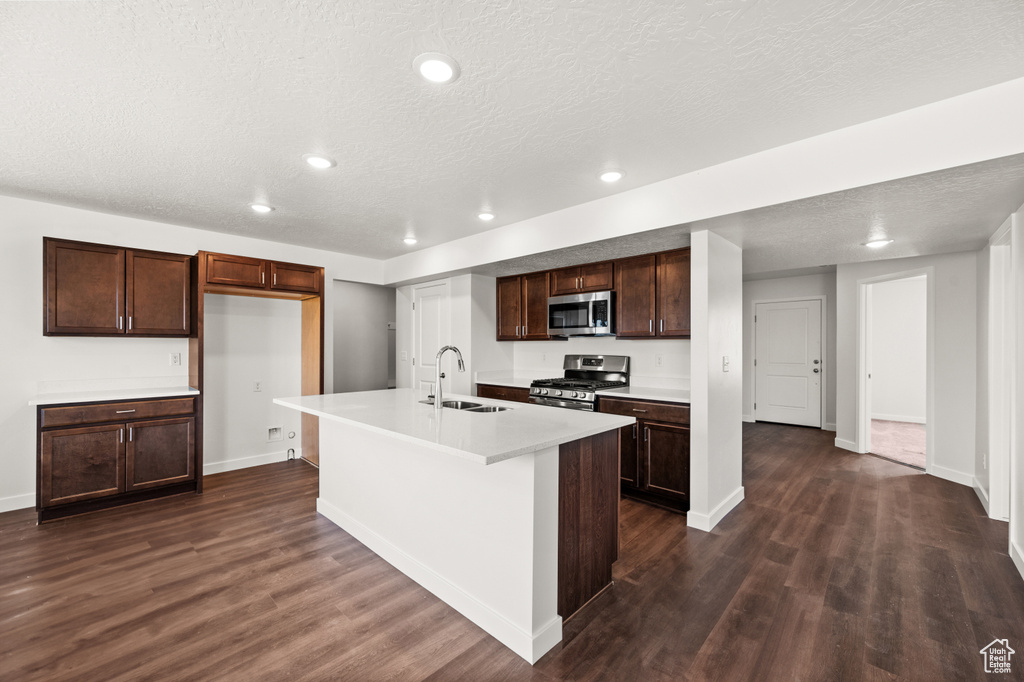 Kitchen with a textured ceiling, dark hardwood / wood-style floors, sink, an island with sink, and appliances with stainless steel finishes