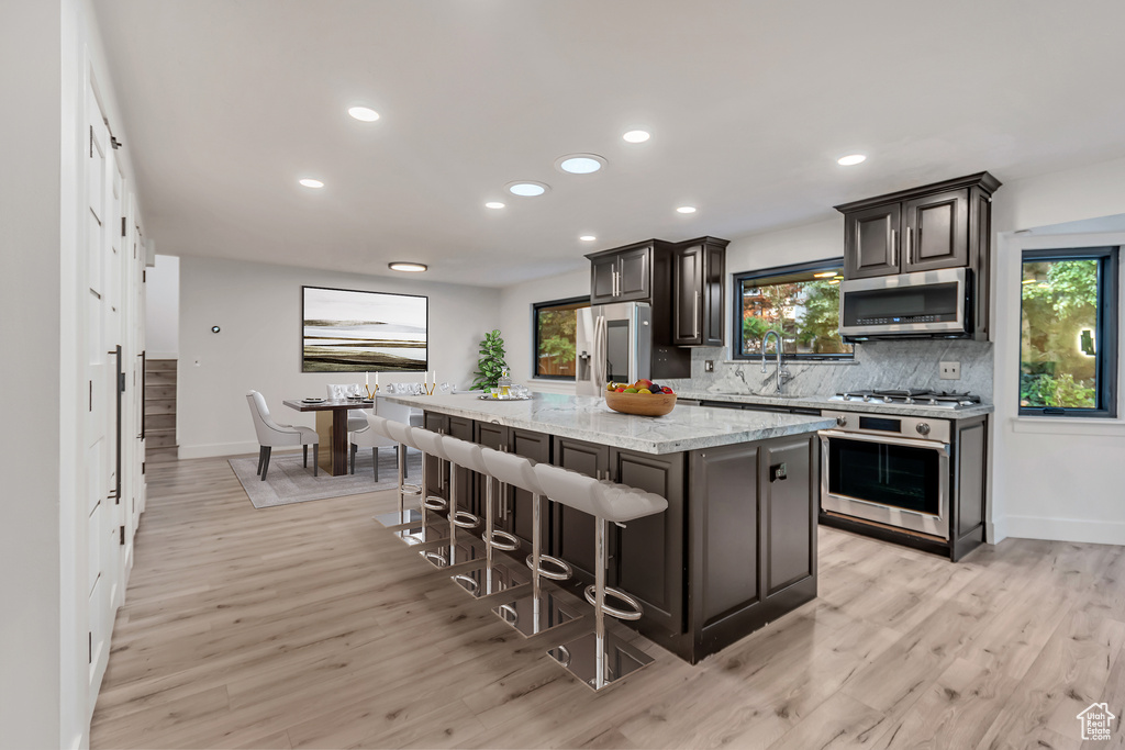 Kitchen with appliances with stainless steel finishes, light wood-type flooring, a kitchen island, and a kitchen breakfast bar