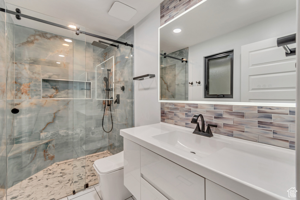 Bathroom with decorative backsplash, vanity, toilet, and a shower with shower door