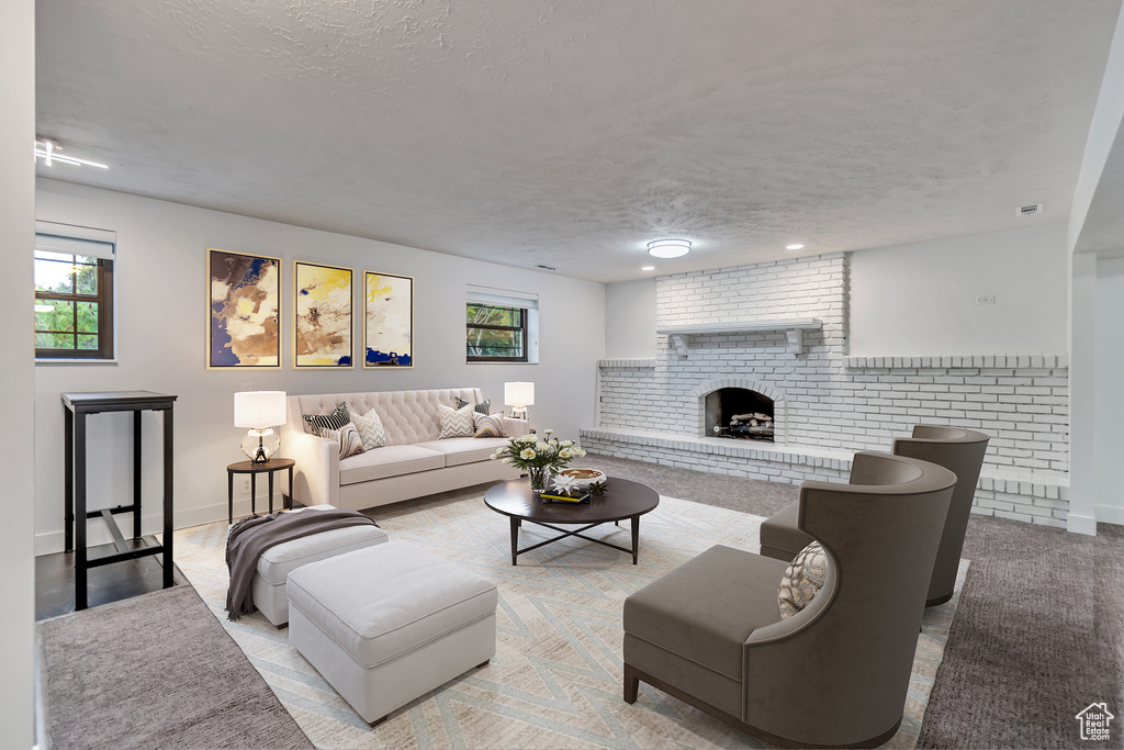 Carpeted living room featuring a brick fireplace, a textured ceiling, and brick wall