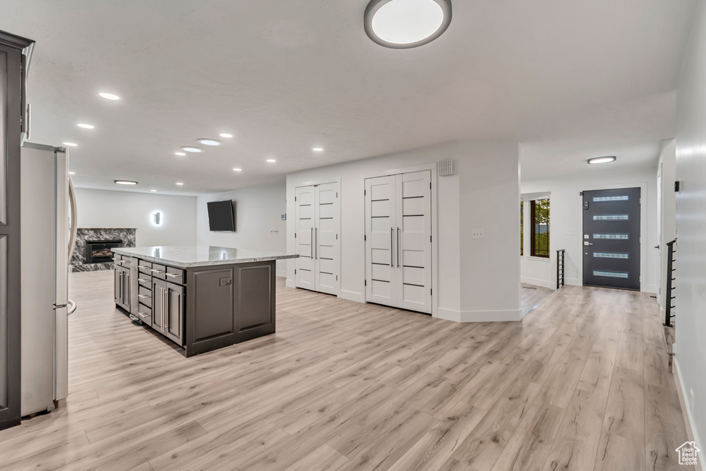 Kitchen with light wood-type flooring, a premium fireplace, a center island, and stainless steel fridge