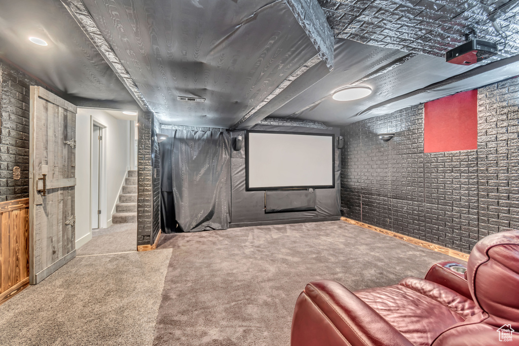 Carpeted cinema room featuring brick wall