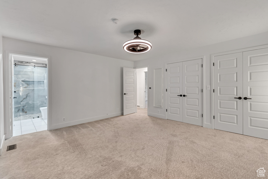 Unfurnished bedroom with light carpet, multiple closets, ensuite bathroom, and ceiling fan