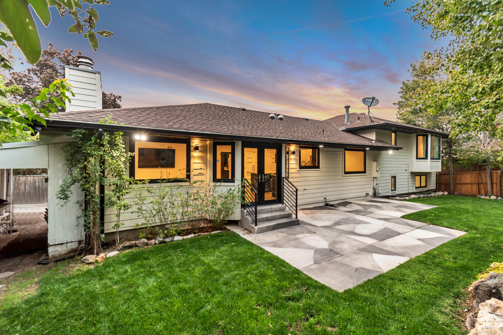 Back house at dusk featuring a lawn and a patio area