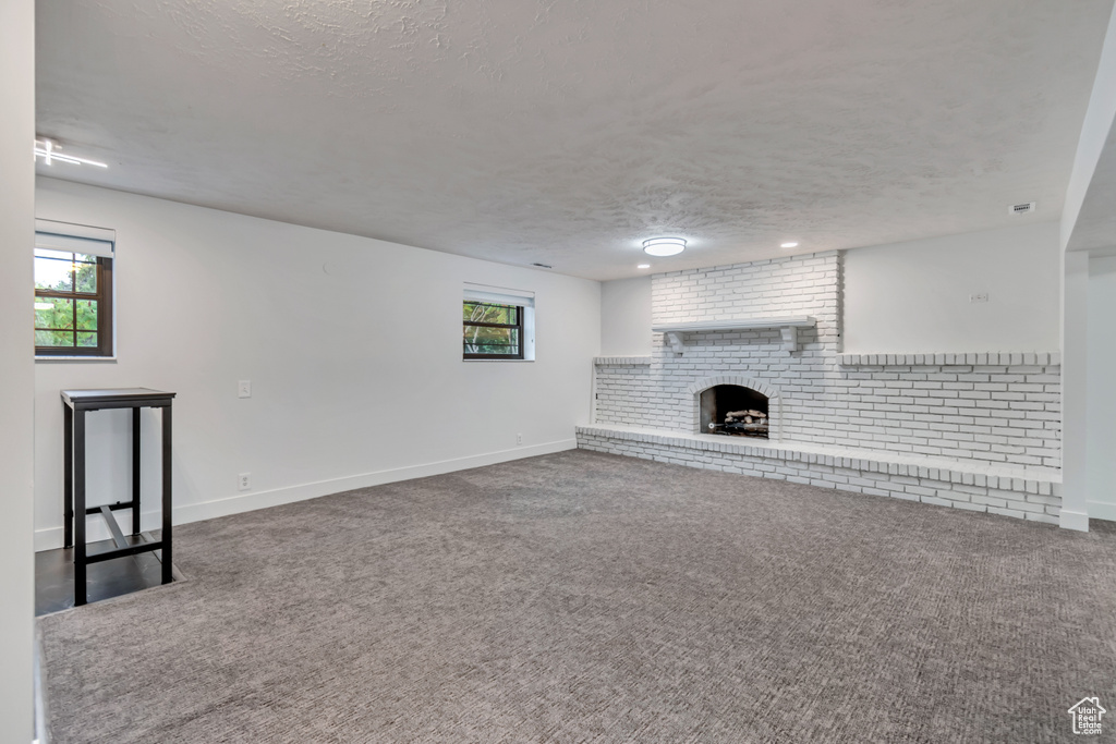 Unfurnished living room with a textured ceiling, carpet flooring, a wealth of natural light, and a brick fireplace