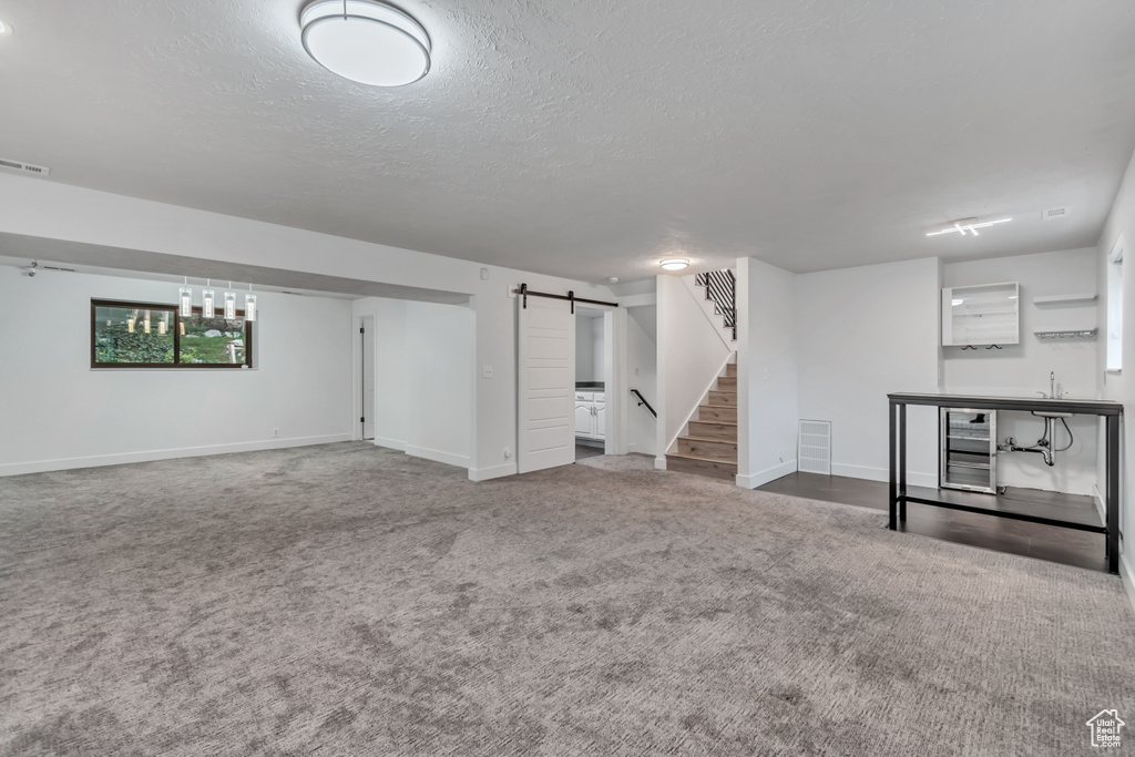 Basement with a textured ceiling, sink, beverage cooler, carpet floors, and a barn door