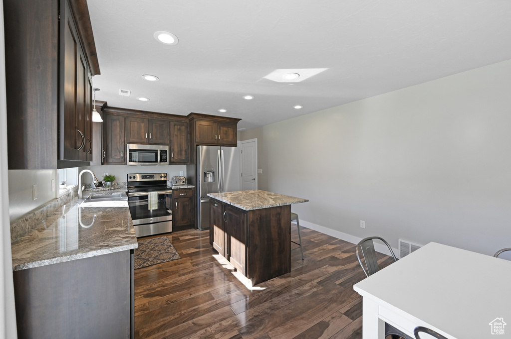 Kitchen featuring appliances with stainless steel finishes, a kitchen island, light stone countertops, dark hardwood / wood-style floors, and sink