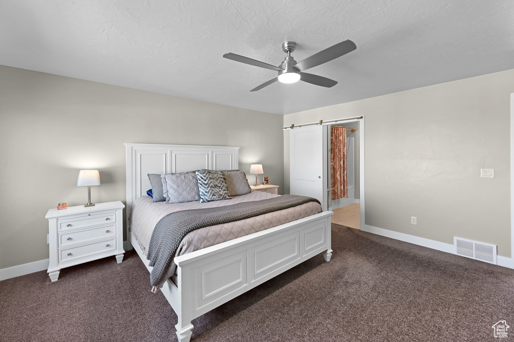 Bedroom with a textured ceiling, a barn door, dark colored carpet, and ceiling fan