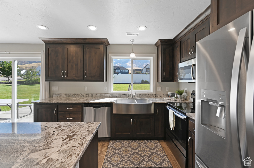 Kitchen with light stone counters, appliances with stainless steel finishes, light wood-type flooring, and a wealth of natural light