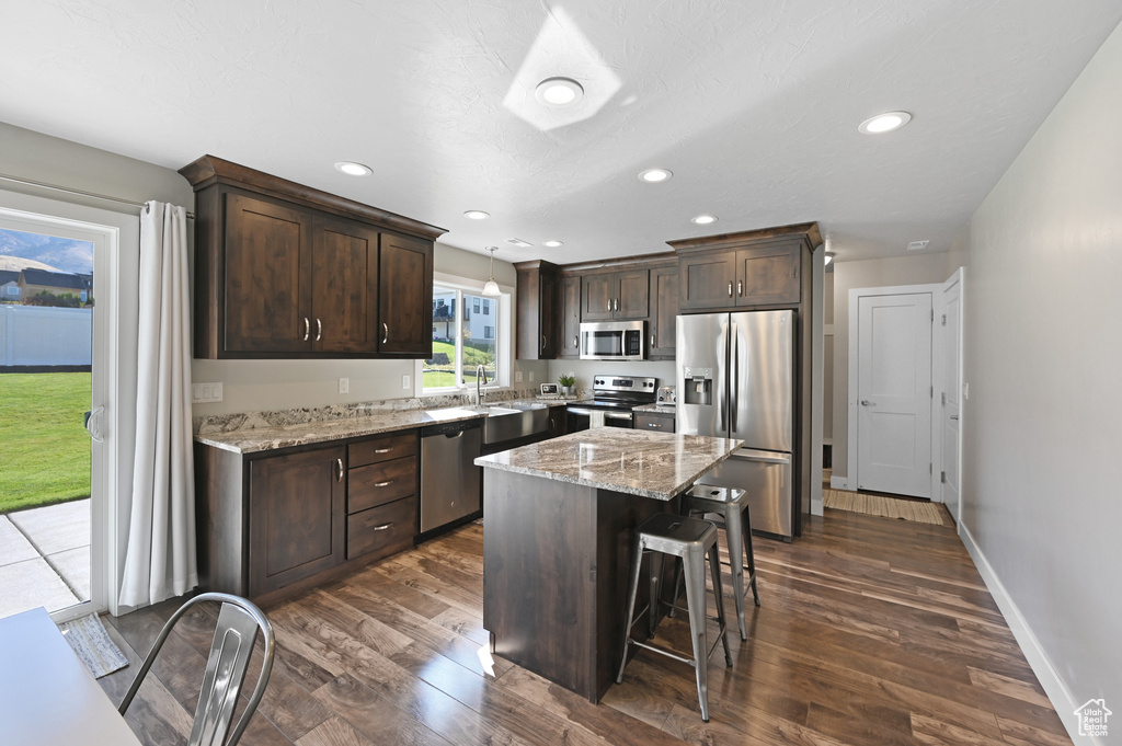 Kitchen featuring appliances with stainless steel finishes, dark brown cabinetry, a kitchen island, and dark hardwood / wood-style floors