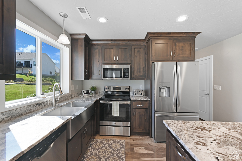 Kitchen with light stone counters, dark wood-type flooring, sink, appliances with stainless steel finishes, and decorative light fixtures