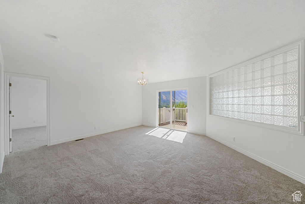 Spare room with a textured ceiling, a chandelier, and light colored carpet