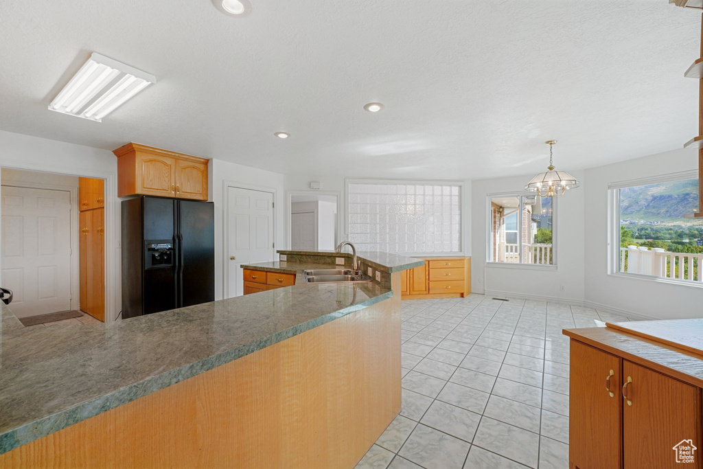 Kitchen with sink, an inviting chandelier, black fridge with ice dispenser, decorative light fixtures, and light tile patterned floors