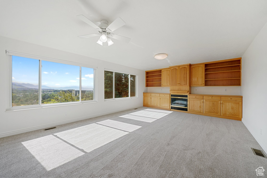 Unfurnished living room featuring light carpet, beverage cooler, a mountain view, and ceiling fan