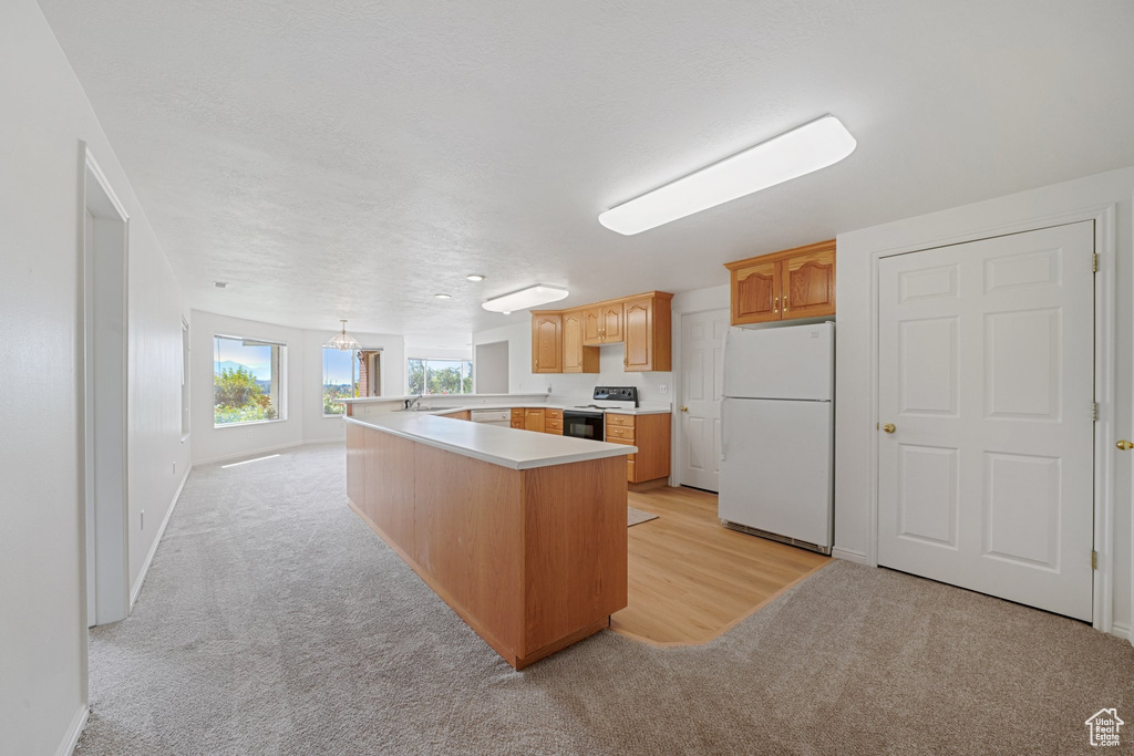 Kitchen featuring electric range, light colored carpet, hanging light fixtures, a kitchen island, and white fridge