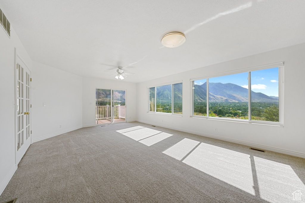 Carpeted empty room featuring ceiling fan, a mountain view, and a wealth of natural light