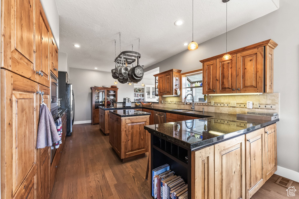 Kitchen with kitchen peninsula, a textured ceiling, decorative light fixtures, dark hardwood / wood-style floors, and a center island